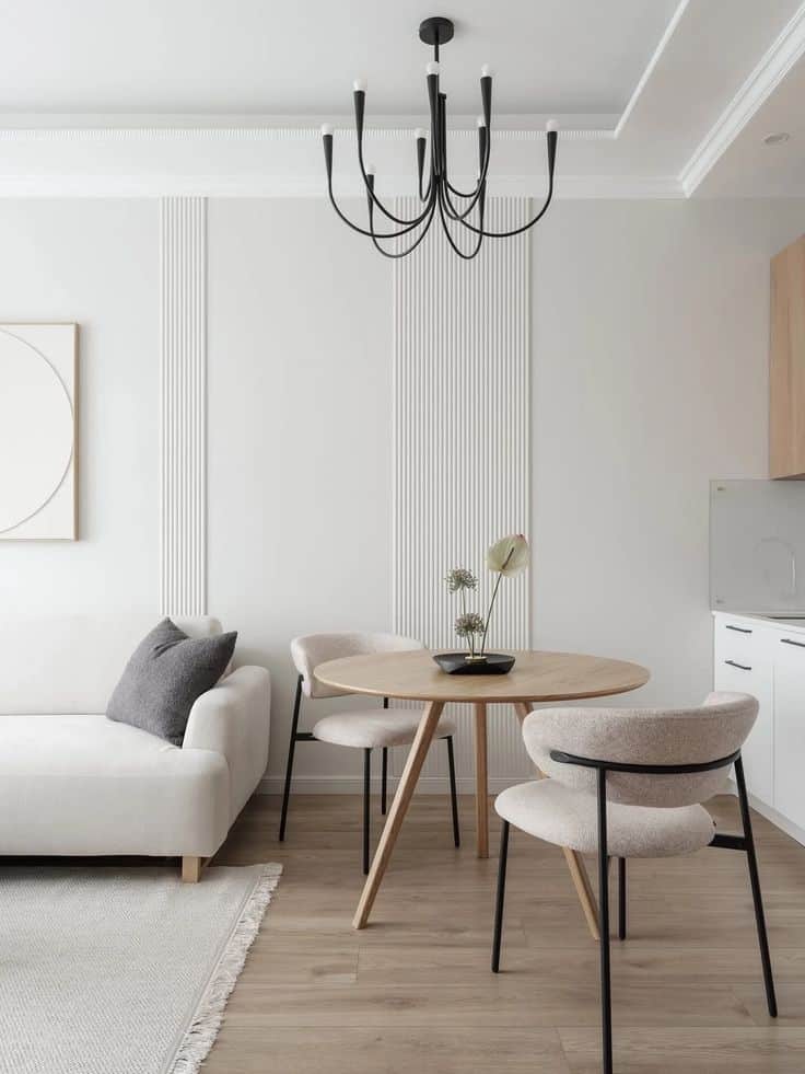 Minimalist living room with a white sofa, round wooden table, modern chandelier, and neutral decor. Bright and chic interior design.