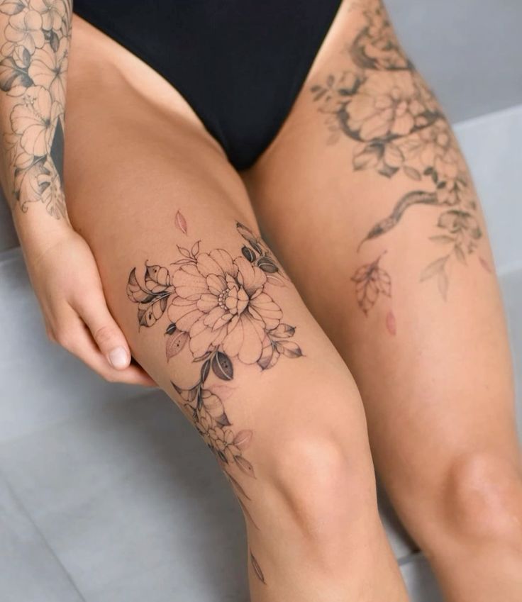 _ 3 Floral thigh tattoos featuring detailed flowers and leaves on a person wearing black swimwear, showcasing intricate body art design. | Sky Rye Design Floral thigh tattoos featuring detailed flowers and leaves on a person wearing black swimwear, showcasing intricate body art design. female thigh tattoo designs