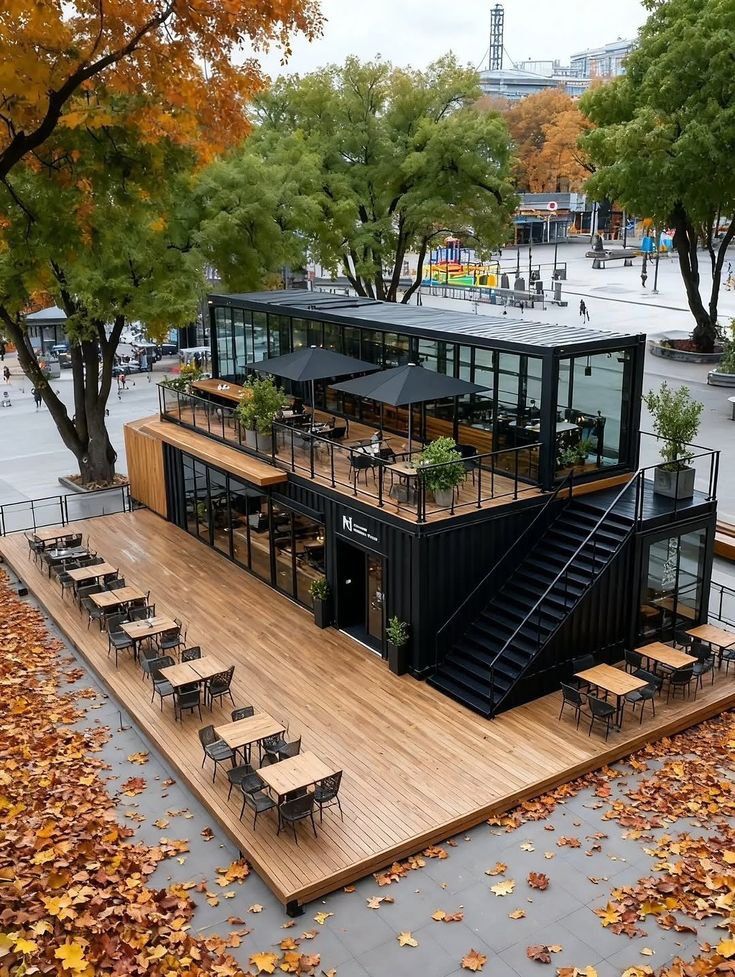 _ 3 Modern container cafe surrounded by autumn leaves, featuring outdoor seating and a rooftop terrace with black umbrellas. | Sky Rye Design Modern container cafe surrounded by autumn leaves, featuring outdoor seating and a rooftop terrace with black umbrellas.