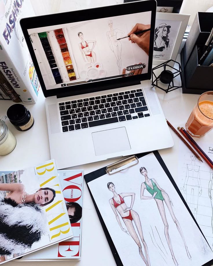 _ 3 Fashion design workspace with laptop, fashion sketches, magazines, and juice, showcasing creative process and inspiration. | Sky Rye Design Fashion design workspace with laptop, fashion sketches, magazines, and juice, showcasing creative process and inspiration.