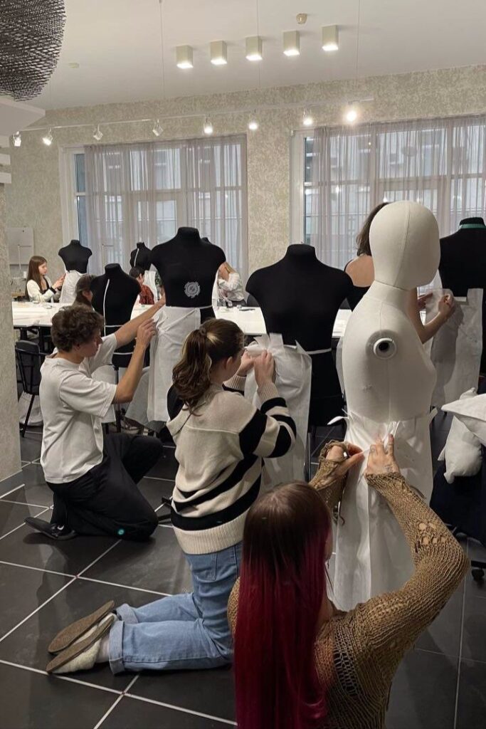Fashion design students creating garments on mannequins in a classroom setting, focusing on draping techniques and teamwork.