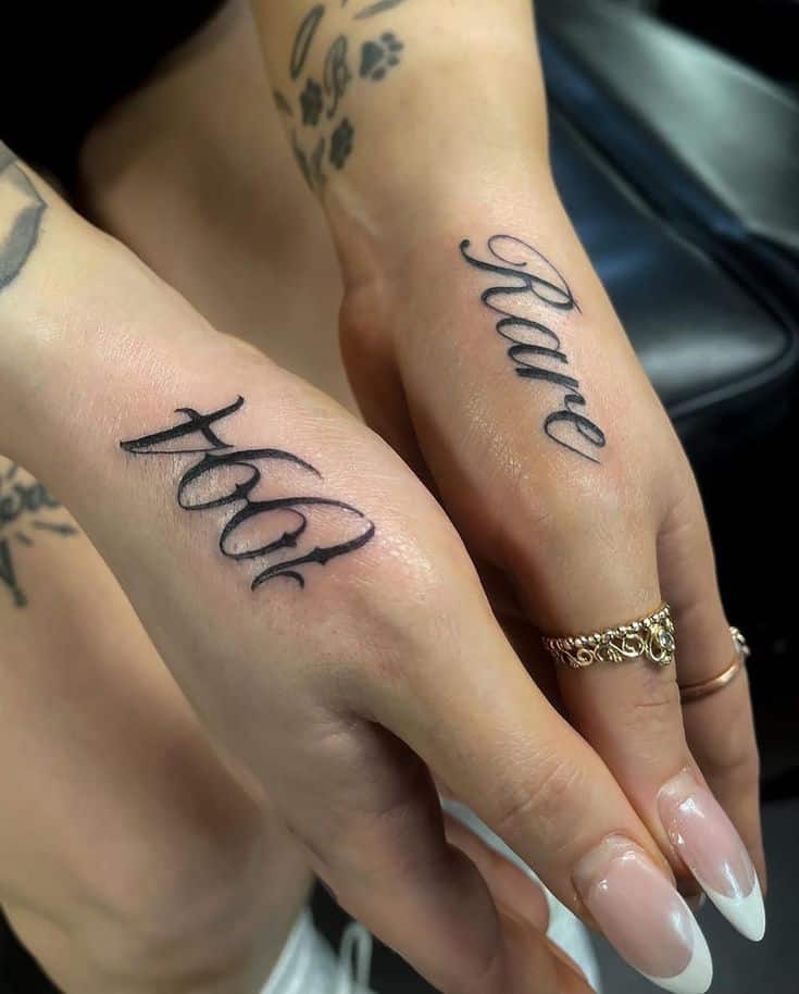 Close-up of hands displaying elegant Rare and free script tattoos with manicured nails and stylish rings.