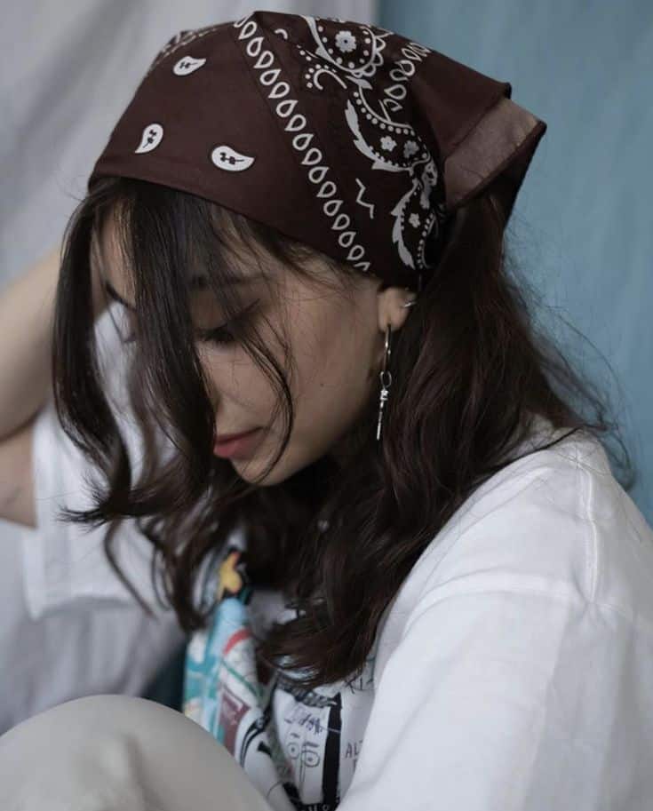 _ 31 Young woman with a brown bandana and curly hair, wearing a graphic white t-shirt, gazing down thoughtfully. | Sky Rye Design Young woman with a brown bandana and curly hair, wearing a graphic white t-shirt, gazing down thoughtfully.