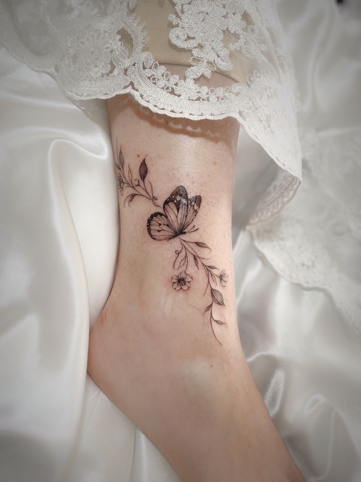 _ 36 Delicate butterfly and floral tattoo on ankle, captured against lace fabric backdrop; intricate ink design on woman's skin. | Sky Rye Design Delicate butterfly and floral tattoo on ankle, captured against lace fabric backdrop; intricate ink design on woman's skin.