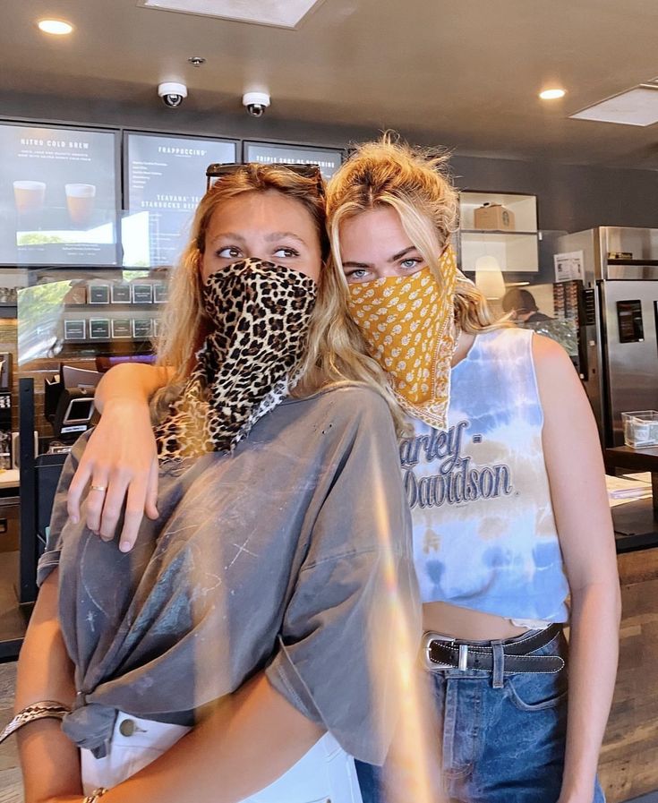 Screenshot Two women in a cafe wearing stylish bandanas as masks, one with leopard print and the other with a yellow pattern, posing together. | Sky Rye Design Two women in a cafe wearing stylish bandanas as masks, one with leopard print and the other with a yellow pattern, posing together.