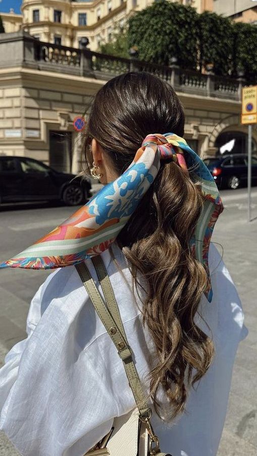_ 39 Woman with long wavy hair in a colorful scarf walks on a sunny city street, wearing a white shirt and carrying a beige bag. | Sky Rye Design Woman with long wavy hair in a colorful scarf walks on a sunny city street, wearing a white shirt and carrying a beige bag.