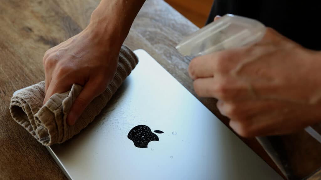 3da5942a-3b53-4202-a5b2-f044730c94e8 Cleaning a silver laptop with a cloth and spray bottle on a wooden table, showcasing maintenance and care for electronic devices. | Sky Rye Design Cleaning a silver laptop with a cloth and spray bottle on a wooden table, showcasing maintenance and care for electronic devices.