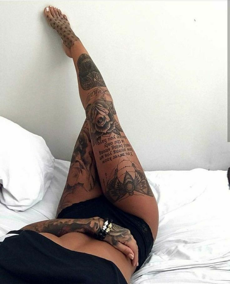 _ 4 Person laying on a bed with elaborately tattooed legs, featuring intricate designs and a decorative armband, set against a white background. | Sky Rye Design Person laying on a bed with elaborately tattooed legs, featuring intricate designs and a decorative armband, set against a white background.