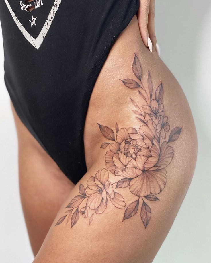 _ 4 Floral thigh tattoo on woman in black swimsuit, featuring peonies and leaves in delicate linework. | Sky Rye Design Floral thigh tattoo on woman in black swimsuit, featuring peonies and leaves in delicate linework.