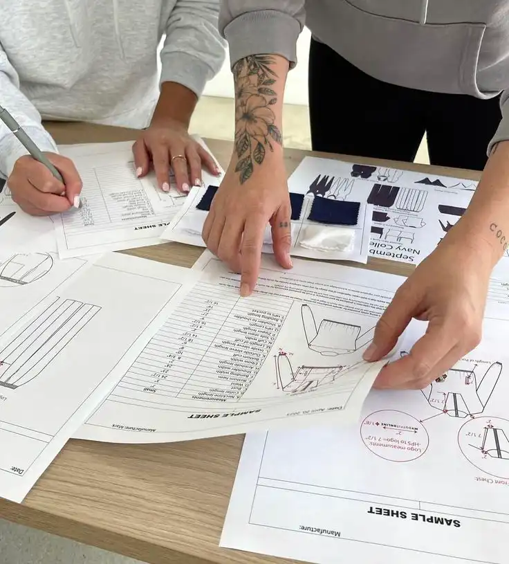 People reviewing and discussing design blueprints and fabric samples at a table, engaging in a collaborative creative process.