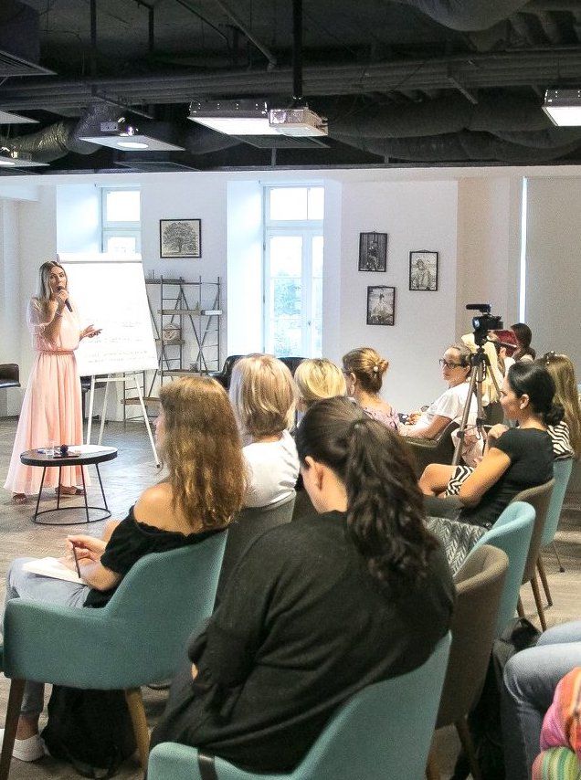 _ 4 A woman leads a presentation in front of a group in a modern conference room, with attendees listening attentively. | Sky Rye Design A woman leads a presentation in front of a group in a modern conference room, with attendees listening attentively.