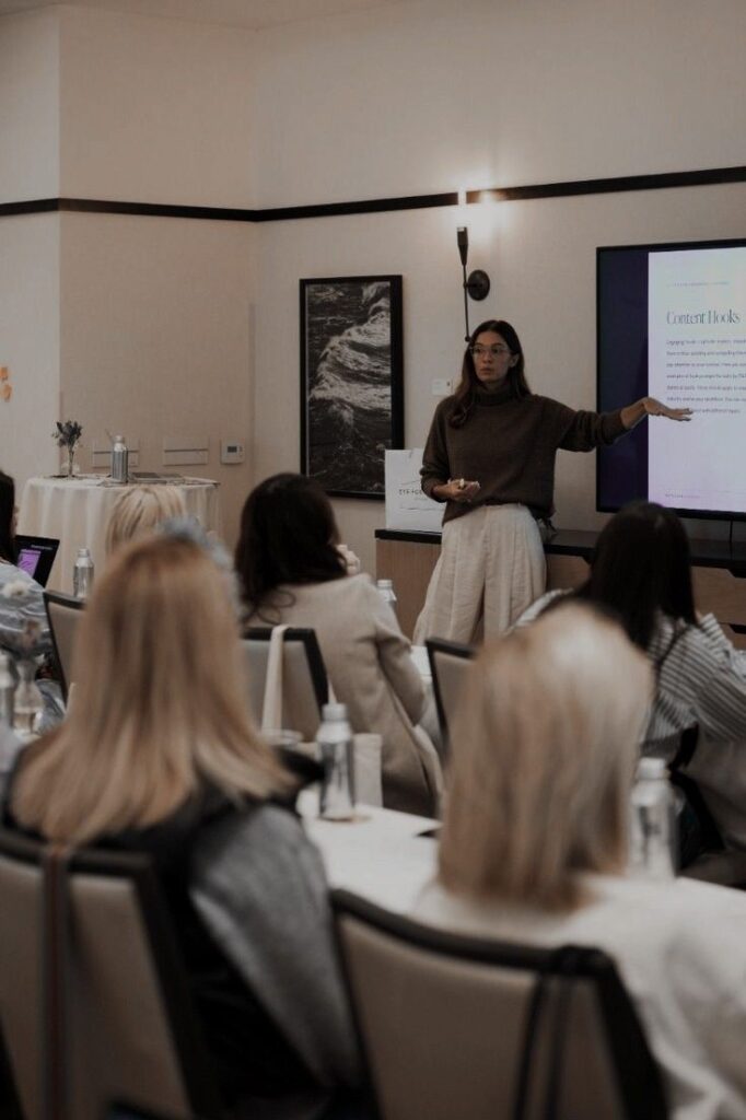 _ 4 Woman giving a presentation on content hacks to a seated audience in a conference room. | Sky Rye Design Woman giving a presentation on content hacks to a seated audience in a conference room.