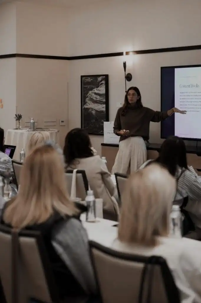 Woman giving a presentation on content hacks to a seated audience in a conference room.