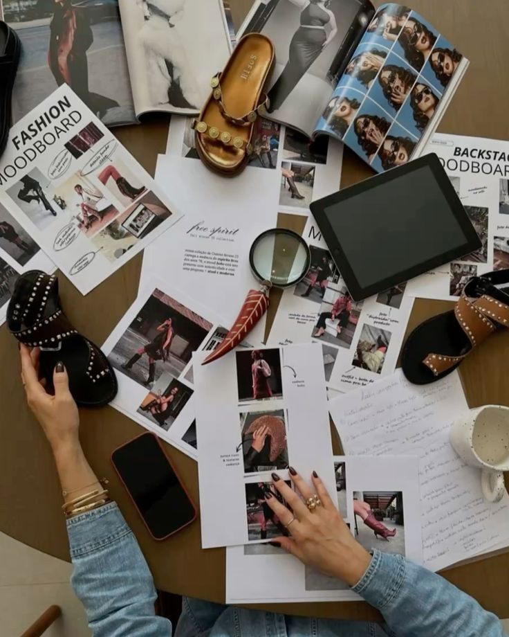 Fashion moodboard and accessories on a table with magazines, shoes, and a tablet, showcasing creative inspiration and design elements.