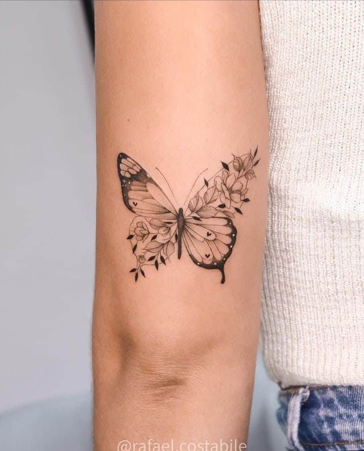 _ 40 Butterfly tattoo with floral details on a person's arm, showcased on a background of a light knitted sweater and denim. | Sky Rye Design Butterfly tattoo with floral details on a person's arm, showcased on a background of a light knitted sweater and denim.