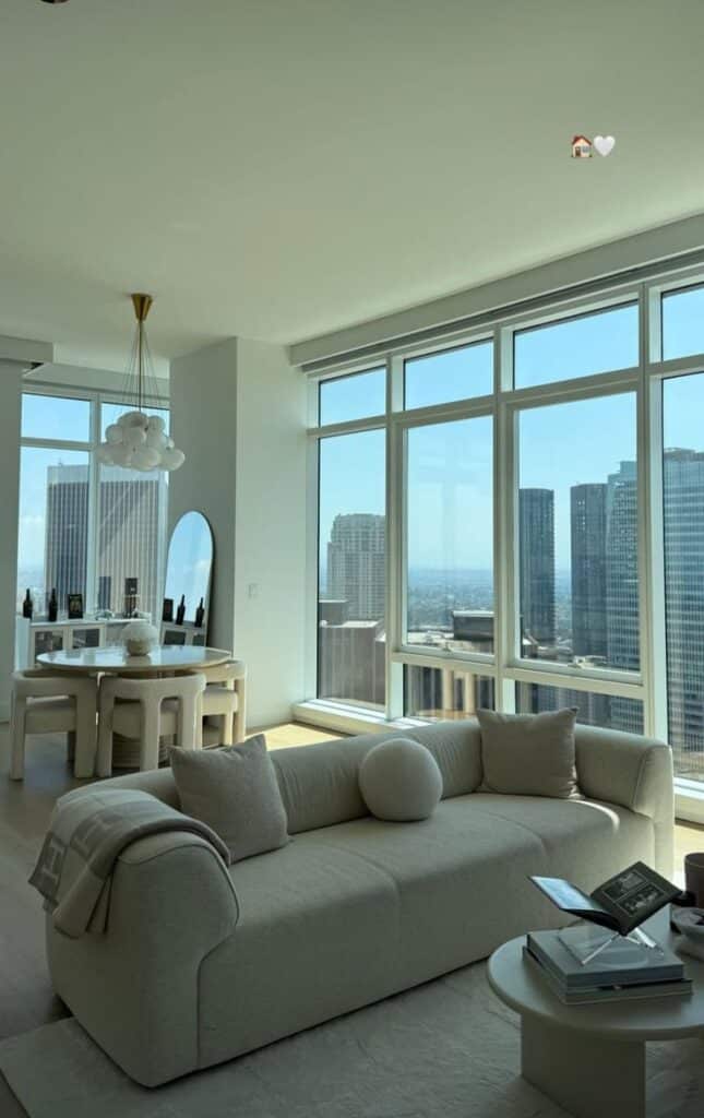 4170d70c-e1dd-4755-b8f7-e36edc198969 Modern luxury living room with beige sofa, large windows, city skyline views, and stylish dining area in a high-rise apartment. | Sky Rye Design Modern luxury living room with beige sofa, large windows, city skyline views, and stylish dining area in a high-rise apartment.