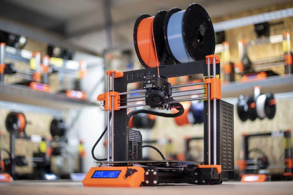3D printer with orange accents and dual filament spools, ready for use on a wooden surface in a workshop setting. Gifts for 3D Printing