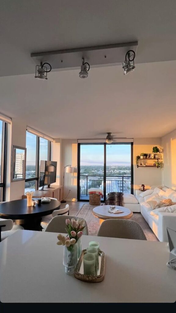 43a0c3c5-51bf-4c15-8ab2-f79796990a3c Modern living room with large windows, stylish decor, cozy white sofa, and scenic city view at sunset. | Sky Rye Design Modern living room with large windows, stylish decor, cozy white sofa, and scenic city view at sunset.