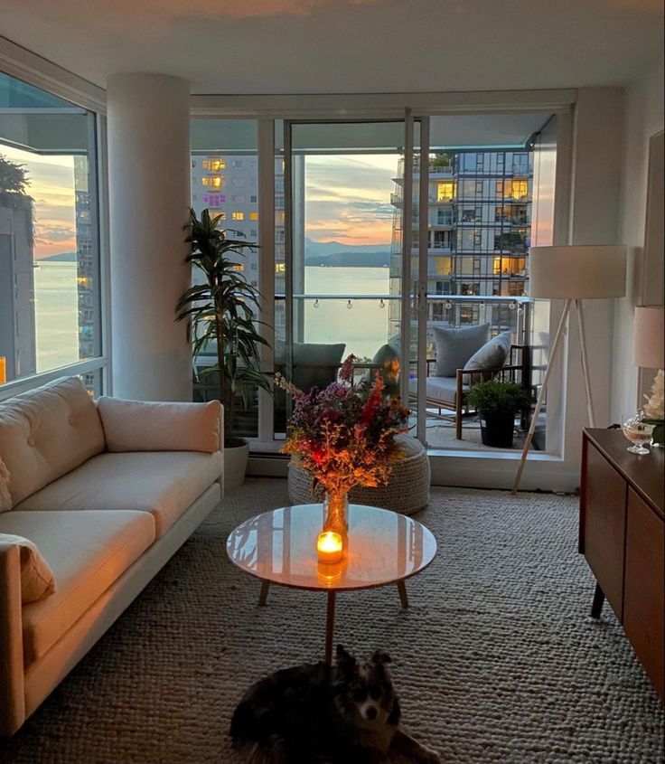 44d96fa6-898f-464c-97a0-689ec99c2539 Cozy living room with a sunset view, featuring a sofa, candle-lit coffee table with flowers, and glass doors leading to a balcony with seating. | Sky Rye Design Cozy living room with a sunset view, featuring a sofa, candle-lit coffee table with flowers, and glass doors leading to a balcony with seating.