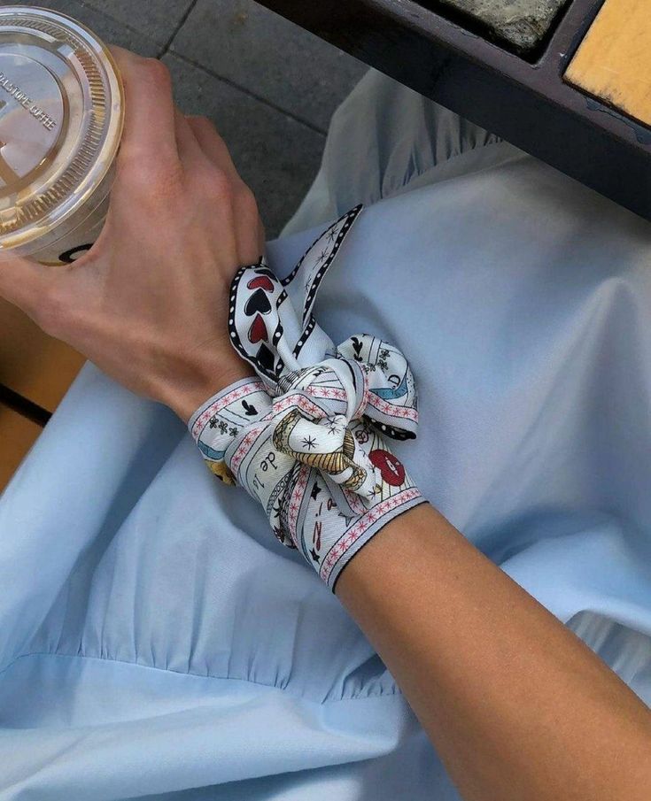 _ 45 Person holding an iced coffee wearing a patterned scarf bracelet, dressed in a light blue outfit. Fashionable and stylish accessory choice. | Sky Rye Design Person holding an iced coffee wearing a patterned scarf bracelet, dressed in a light blue outfit. Fashionable and stylish accessory choice.