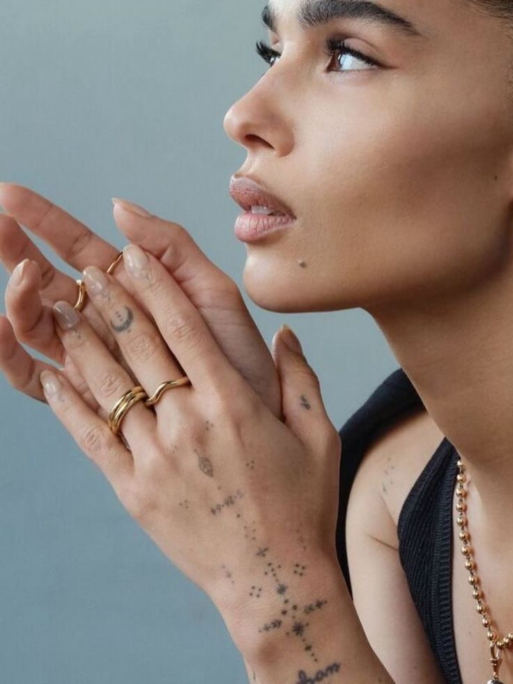 Profile of a person with artistic tattoos and gold jewelry on their hands, gazing thoughtfully upwards.