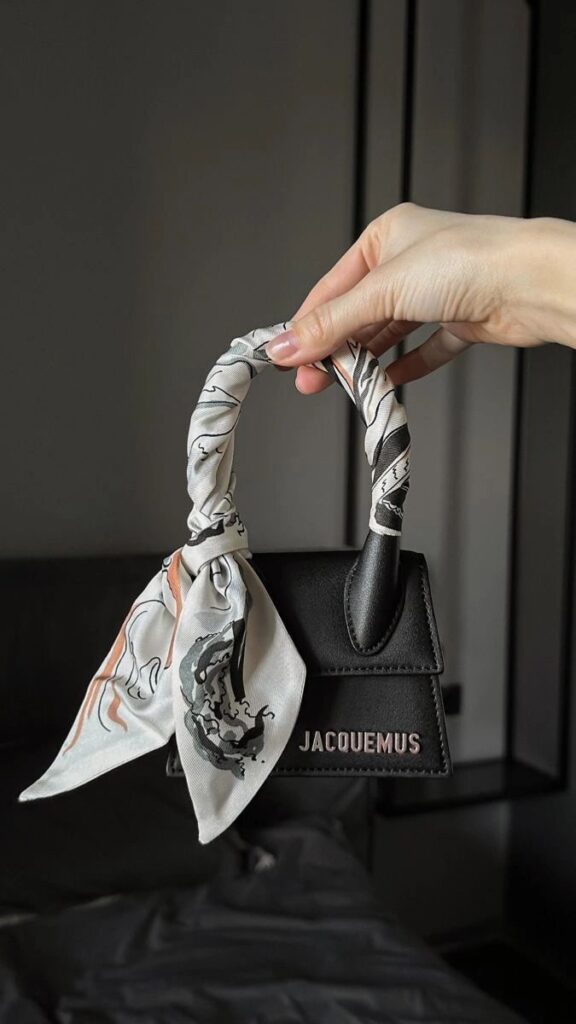 _ 47 Elegant black Jacquemus handbag with a floral-patterned scarf tied on the handle, held by a hand. Perfect for fashion styling. | Sky Rye Design Elegant black Jacquemus handbag with a floral-patterned scarf tied on the handle, held by a hand. Perfect for fashion styling.