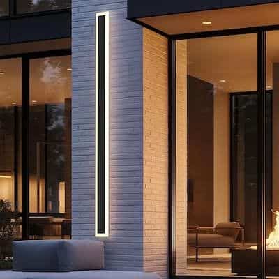 Modern outdoor lighting on a stylish brick wall with a cozy interior view through large glass windows, creating a warm ambiance.