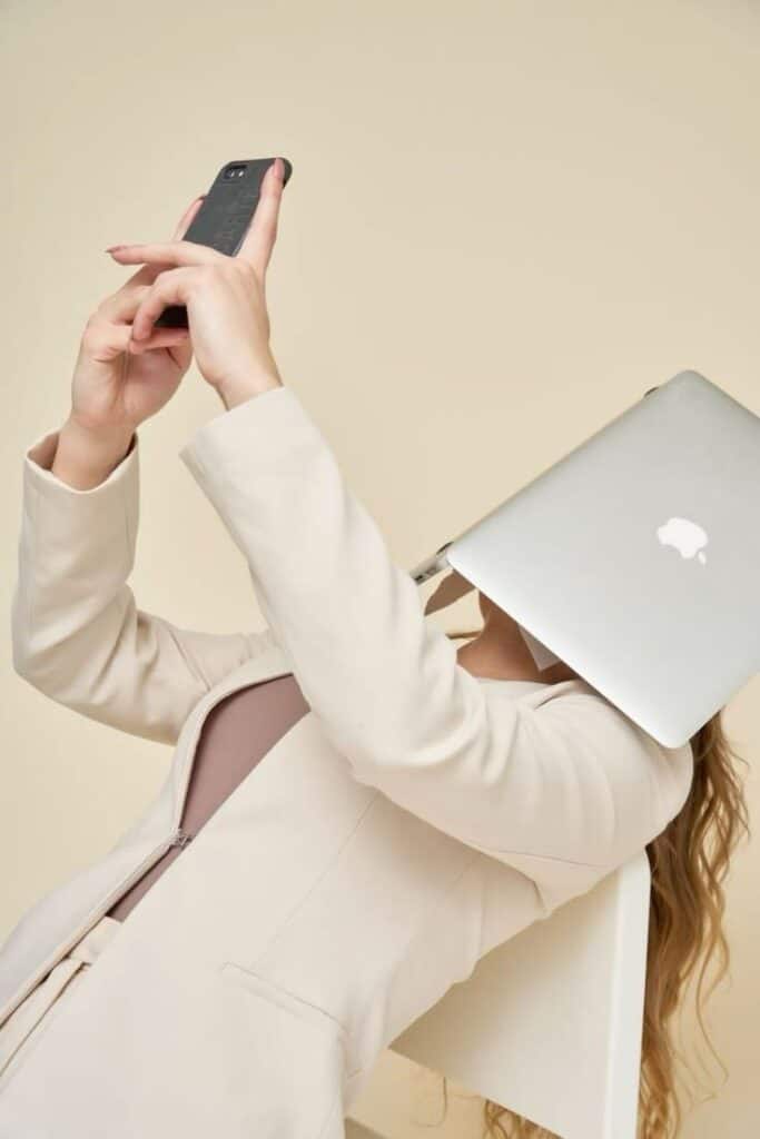 _ 5 Person with laptop on face, taking selfie on phone while sitting, symbolizing technology's overwhelming impact on modern life. | Sky Rye Design Person with laptop on face, taking selfie on phone while sitting, symbolizing technology's overwhelming impact on modern life.