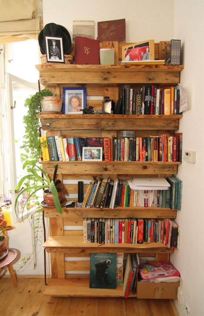 _ 5 Wooden bookshelf filled with a variety of books, framed photos, and potted plants, adding a cozy touch to the home interior. | Sky Rye Design Wooden bookshelf filled with a variety of books, framed photos, and potted plants, adding a cozy touch to the home interior.