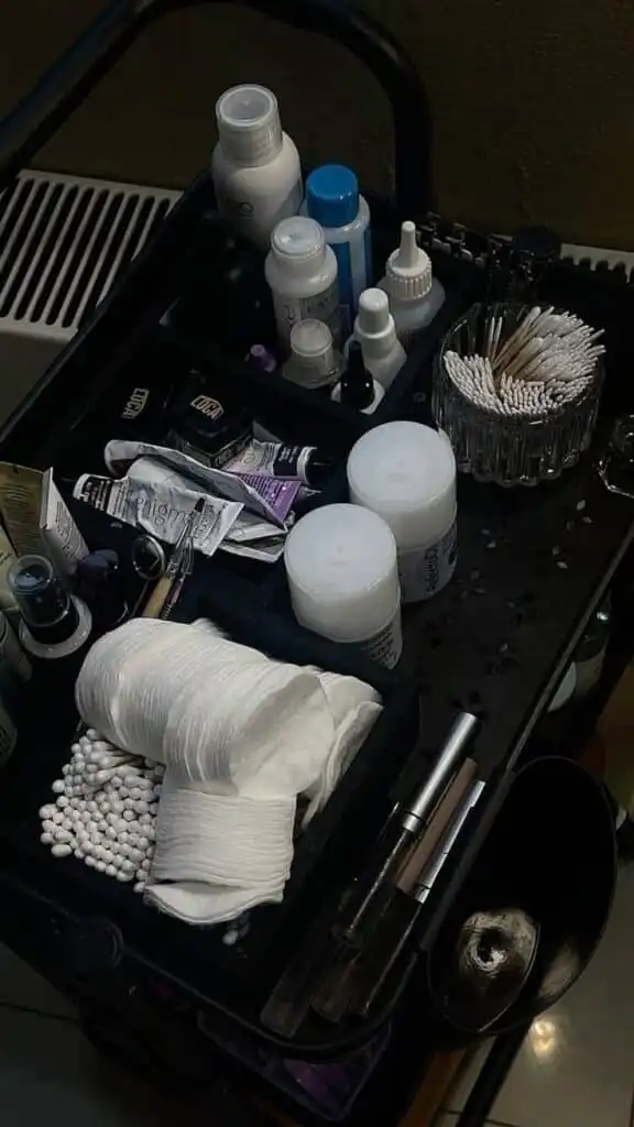 Beauty salon workstation with skincare bottles, cotton pads, and tools organized on a black trolley, ideal for professional treatments.