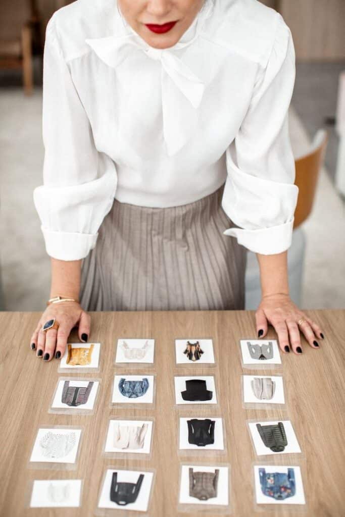 _ 5 Woman in white blouse examines fashion images on table, selecting outfits. Stylish design choice concept with various clothing styles. | Sky Rye Design Woman in white blouse examines fashion images on table, selecting outfits. Stylish design choice concept with various clothing styles.