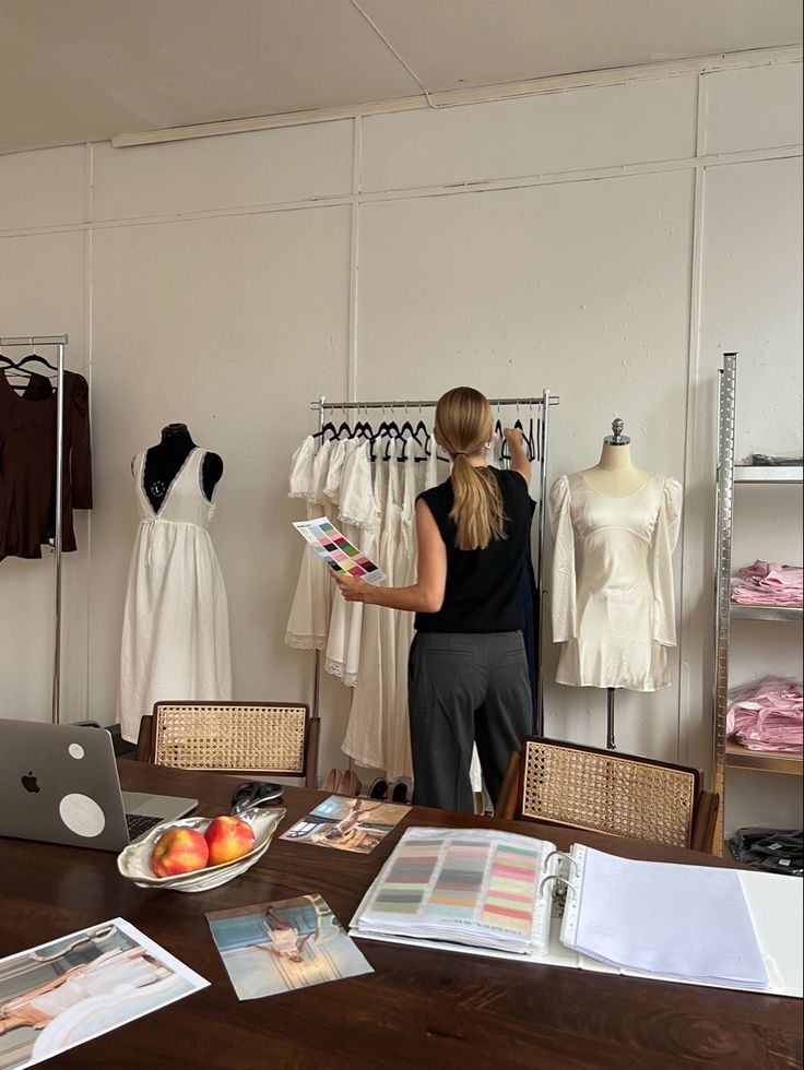 Fashion designer reviewing clothing rack with color swatches in cozy studio, surrounded by sketches and fabric samples on the table.