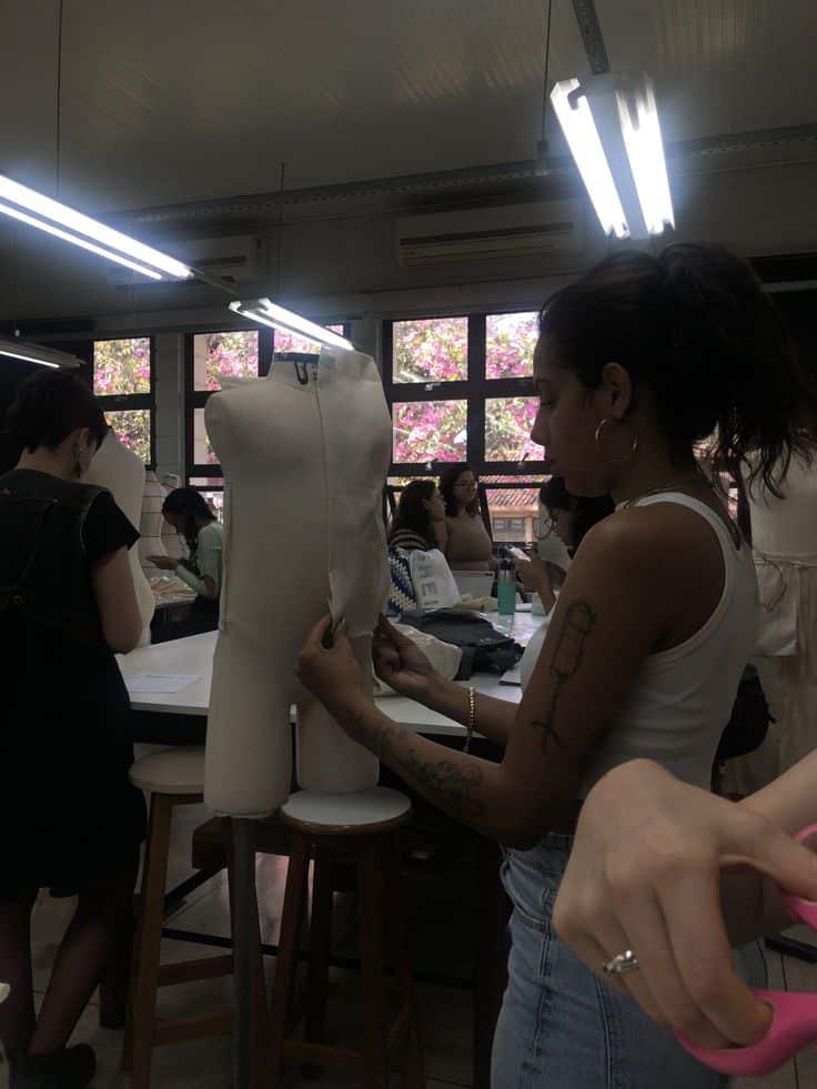 Fashion design students working with mannequins in classroom, focusing on pattern making and sewing projects under bright lighting.