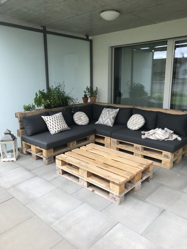 502e747e9a784bc52d295d3da8cc9d90 Outdoor patio with pallet furniture, grey cushions, decorative pillows, and potted plants, creating a cozy modern seating area. | Sky Rye Design Outdoor patio with pallet furniture, grey cushions, decorative pillows, and potted plants, creating a cozy modern seating area.
