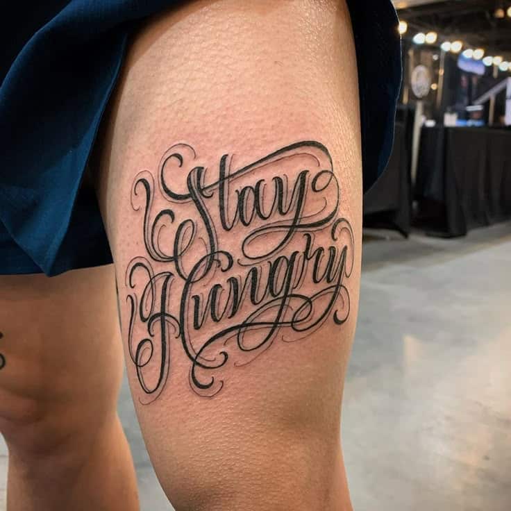 551d19a8-7a4f-4353-84cc-a3c1ee50dd16 Tattoo of Stay Hungry in elegant script on a person's leg at a convention, highlighting motivation and artistic design. | Sky Rye Design Tattoo of Stay Hungry in elegant script on a person's leg at a convention, highlighting motivation and artistic design.
