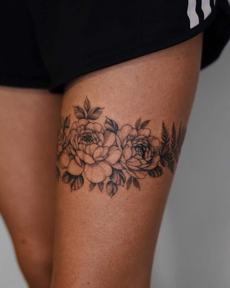 56 Best Thigh Tattoos for Women_ Feminine Fierce and Fearlessly Flawless Floral thigh tattoo featuring detailed roses and leaves on the skin, showcasing intricate black ink artistry against a light background. | Sky Rye Design Floral thigh tattoo featuring detailed roses and leaves on the skin, showcasing intricate black ink artistry against a light background.