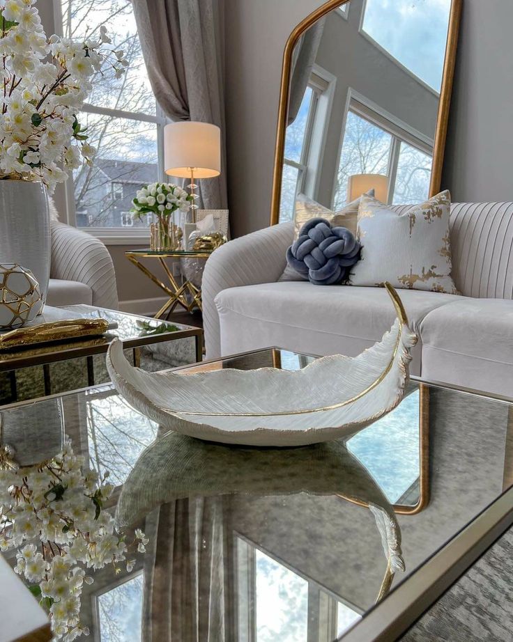 5638bc0e-b25f-407b-a8bb-ee7985bb31f4 Elegant living room with cozy sofas, large mirror, and decorative accents on a glass table. Bright and inviting space with floral touches. | Sky Rye Design Elegant living room with cozy sofas, large mirror, and decorative accents on a glass table. Bright and inviting space with floral touches.