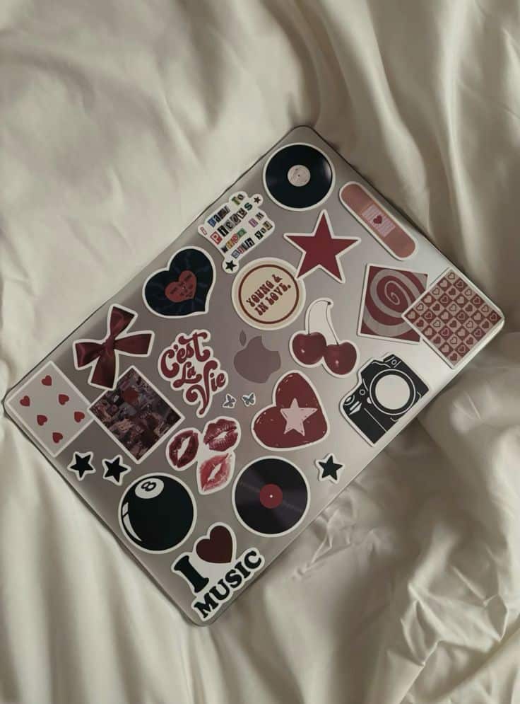 _ 58 Laptop adorned with vibrant stickers featuring music, hearts, and stars on a cozy white bed. Fun and creative expression. | Sky Rye Design Laptop adorned with vibrant stickers featuring music, hearts, and stars on a cozy white bed. Fun and creative expression.
