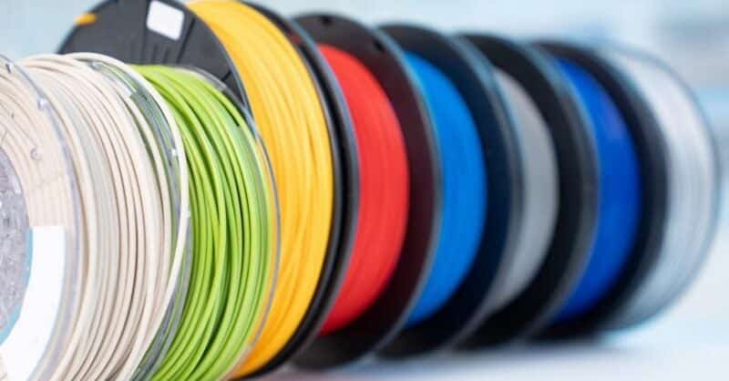 5c1a6473b7365571afaf6703_shutterstock_1145888252 Colorful spools of 3D printer filament in various shades, including white, green, yellow, red, grey, and blue, lined up on a shelf. | Sky Rye Design Colorful spools of 3D printer filament in various shades, including white, green, yellow, red, grey, and blue, lined up on a shelf.
