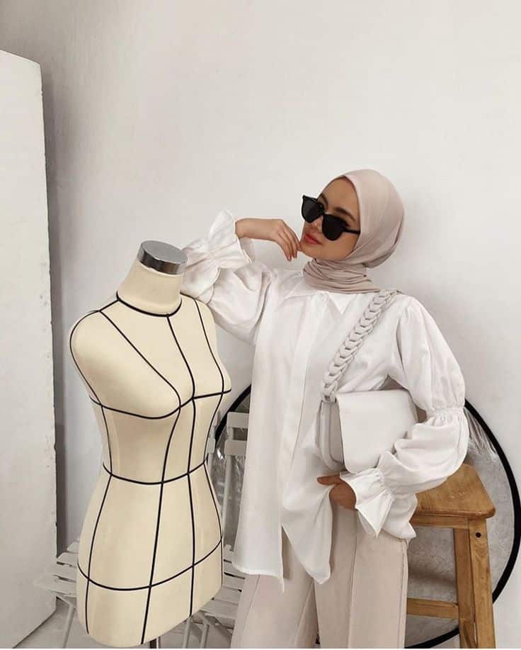 _ 6 Stylish woman in sunglasses and hijab poses confidently beside a dress mannequin, showcasing modern fashion elegance in a chic studio setting. | Sky Rye Design Stylish woman in sunglasses and hijab poses confidently beside a dress mannequin, showcasing modern fashion elegance in a chic studio setting.