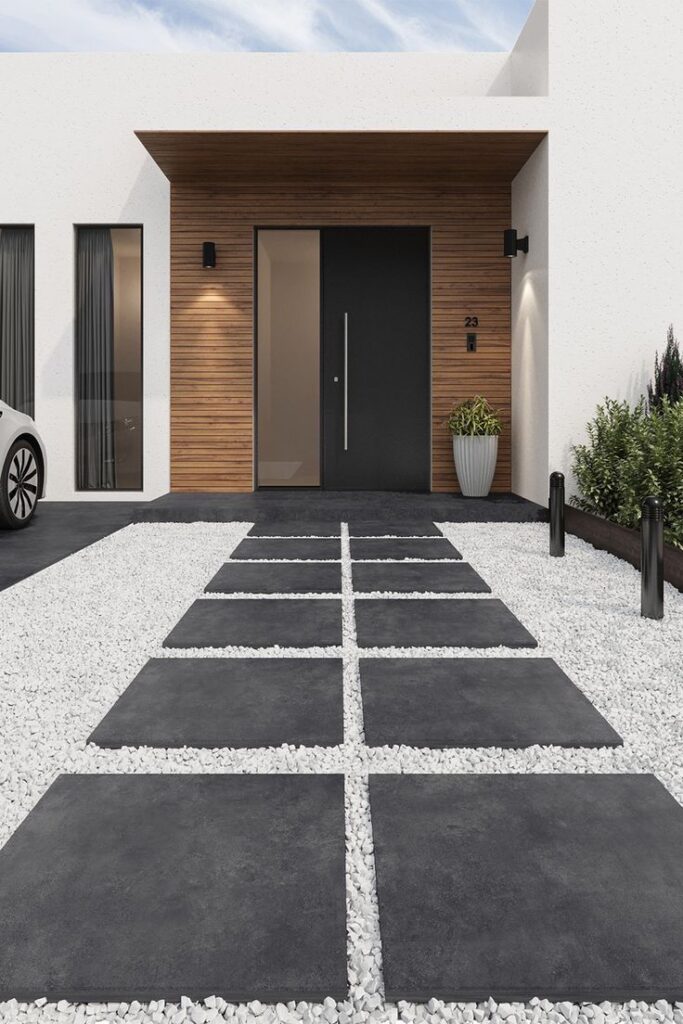 _ 6 Modern minimalist home entrance with a sleek black door, wood paneling, and a geometric stone path surrounded by white gravel landscaping. | Sky Rye Design Modern minimalist home entrance with a sleek black door, wood paneling, and a geometric stone path surrounded by white gravel landscaping.