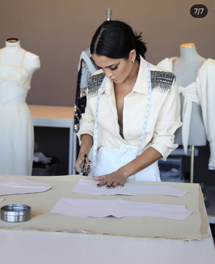 Fashion designer cuts fabric patterns in a studio, surrounded by mannequins, showcasing creativity and attention to detail.