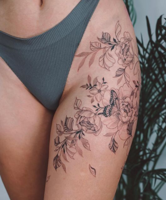 _ 6 Floral thigh tattoo with butterfly, featuring detailed flowers and leaves on skin, next to a person wearing grey underwear. | Sky Rye Design Floral thigh tattoo with butterfly, featuring detailed flowers and leaves on skin, next to a person wearing grey underwear.