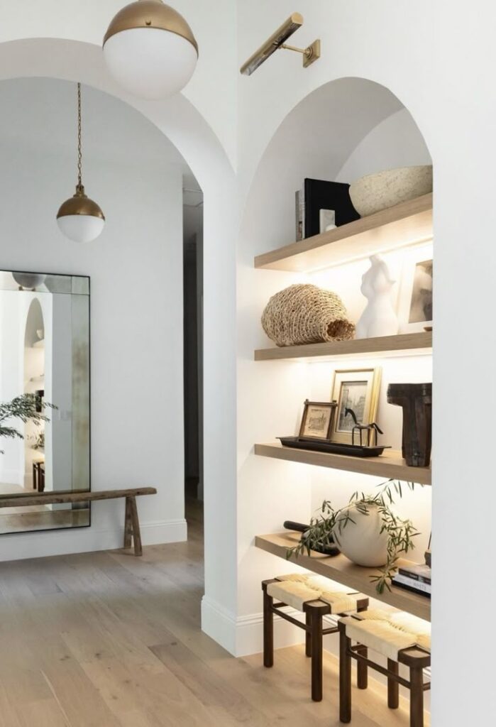 Screenshot Modern interior with arched shelves, artwork, and natural decor. Warm lighting enhances the minimalist design, reflecting cozy elegance. | Sky Rye Design Modern interior with arched shelves, artwork, and natural decor. Warm lighting enhances the minimalist design, reflecting cozy elegance.