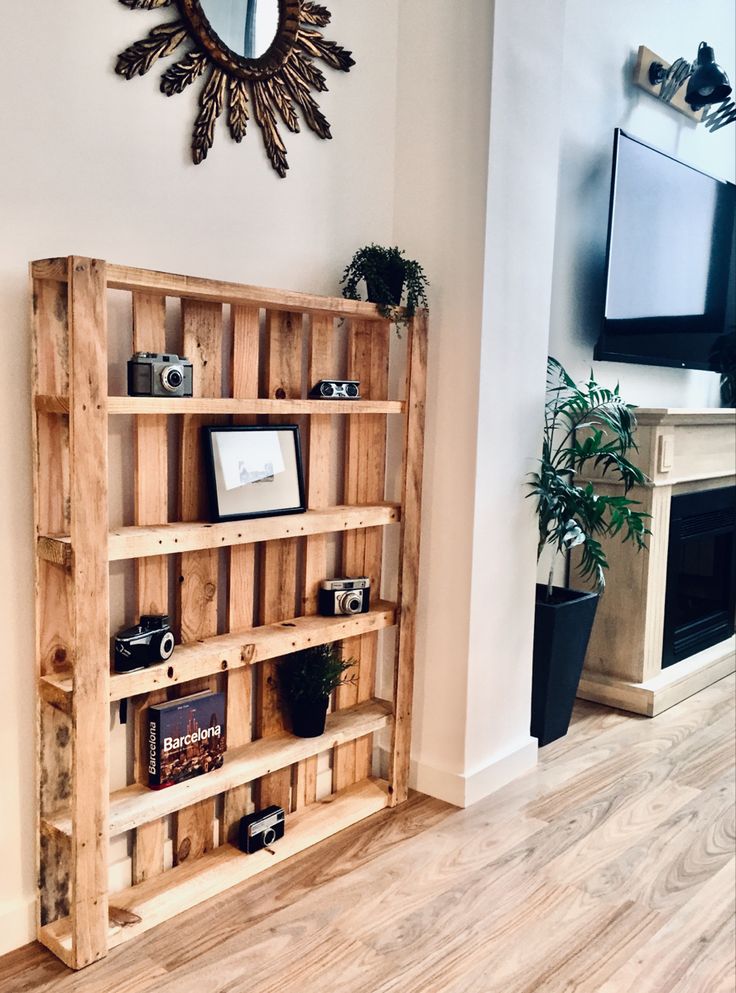 _ 6 Wooden pallet shelf with vintage cameras, plants, and a framed photo, next to a sunburst mirror and modern TV in stylish living room. | Sky Rye Design Wooden pallet shelf with vintage cameras, plants, and a framed photo, next to a sunburst mirror and modern TV in stylish living room.