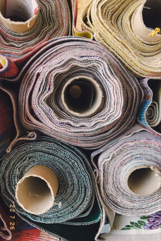 _ 6 Colorful rolls of textile fabric stacked together, showcasing a variety of patterns and textures in a fabric store or workshop setting. | Sky Rye Design Colorful rolls of textile fabric stacked together, showcasing a variety of patterns and textures in a fabric store or workshop setting.