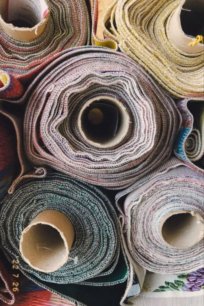 Colorful rolls of textile fabric stacked together, showcasing a variety of patterns and textures in a fabric store or workshop setting.