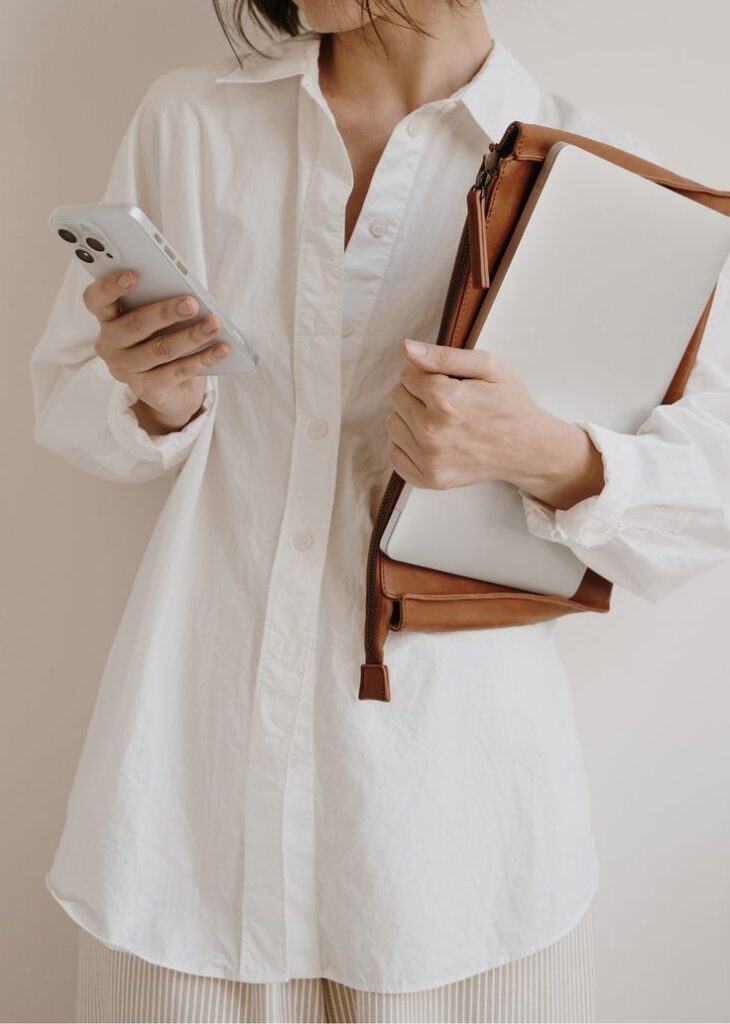 _ 6 Person in a white shirt holds a smartphone and laptop in a brown case, symbolizing modern work and technology on the go. | Sky Rye Design Person in a white shirt holds a smartphone and laptop in a brown case, symbolizing modern work and technology on the go.