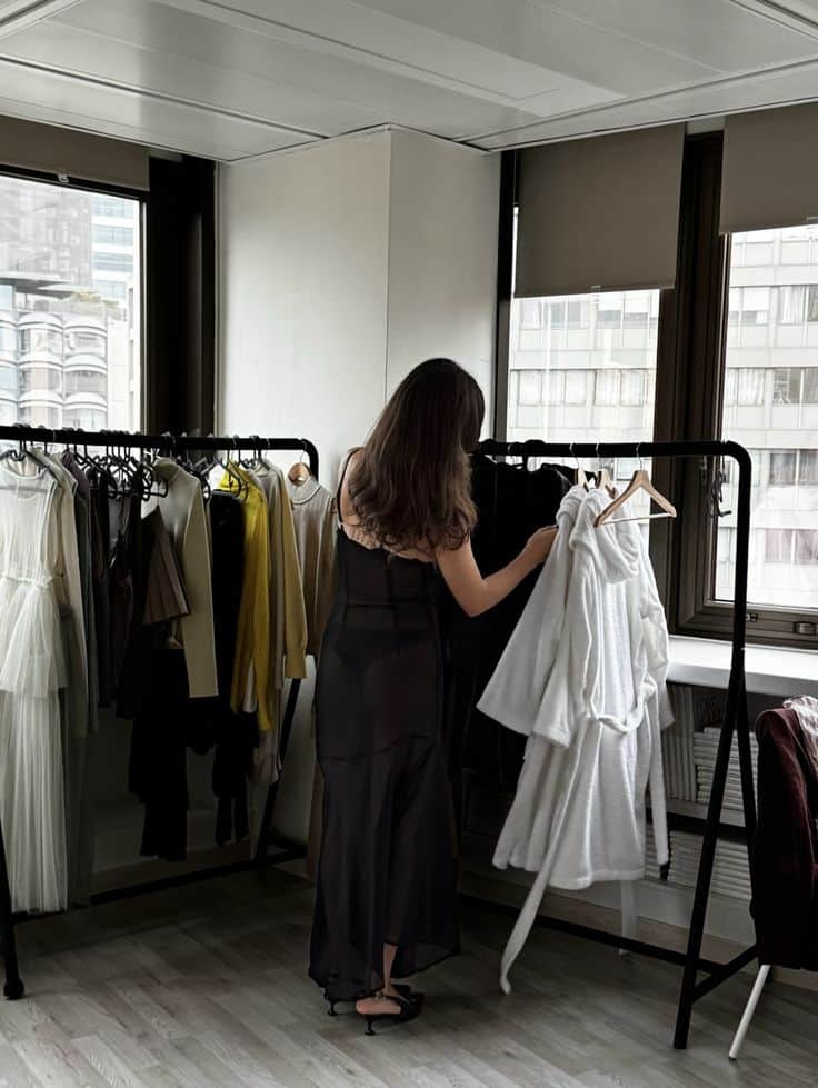 Woman selecting clothes from a rack in a modern office environment, showcasing stylish fashion choices and trendy outfits.