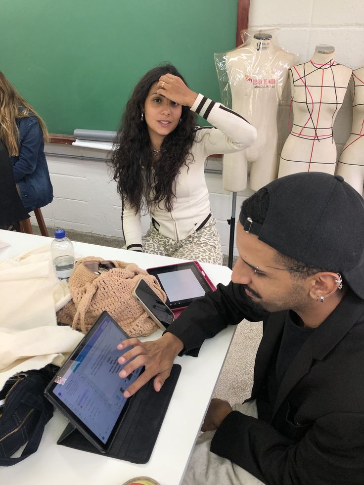 Students collaborating on digital tablets in a fashion design classroom, surrounded by mannequins and creative materials.